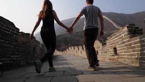 Young woman and man join hands and go along Great Wall of China. Low camera, wide angle shot from floor of stone paved walkway. Tourist pair explore famous Chinese landmark, Mutianyu section