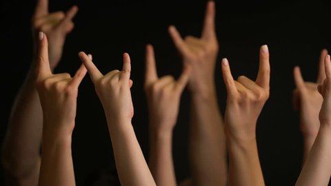 Raising hands with goat gesture or rock sign on black background