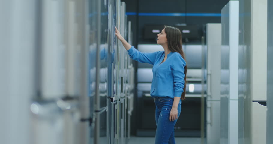 brunette woman in shirt to open the door of the refrigerator in the appliances store and compare with other models to buy the new house Royalty-Free Stock Footage #1028056379