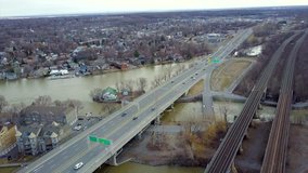 Cinematic drone - aerial footage moving backwards showing a bridge with cars, a train rail over Saint Lawrence River, houses and buildings in Montreal, Quebec, Canada during pre-spring season.