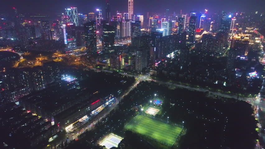 Illuminated Shenzhen City at Night. Futian District. China. Aerial View. Drone Flies Forward, Tilt Up. Reveal Shot