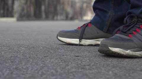 Close-up, feet of a man in sneakers and jeans standing in a city Park Smoking a cigarette. Falling cigarette butt, which a person quits and goes