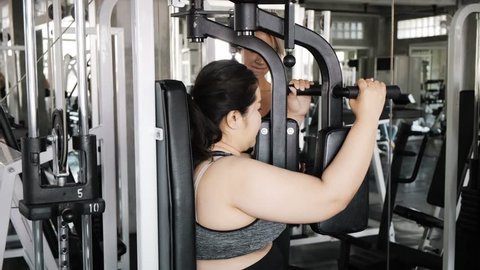 Young fat asian woman trying hard to use pec deck machine in gym. Authentic Fitness lifestyle concept.