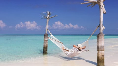 Man in white summer clothes relaxes in a hammock over turquoise, tropical waters