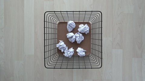 Thrown crumpled paper to basket bin on wooden floor.
