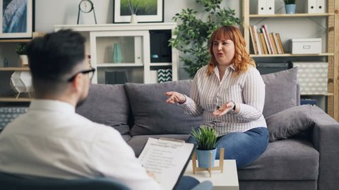 Cheerful obese woman in casual clothing is talking to male psychologist in clinic during session. People are discussing eating disorder and treatment.