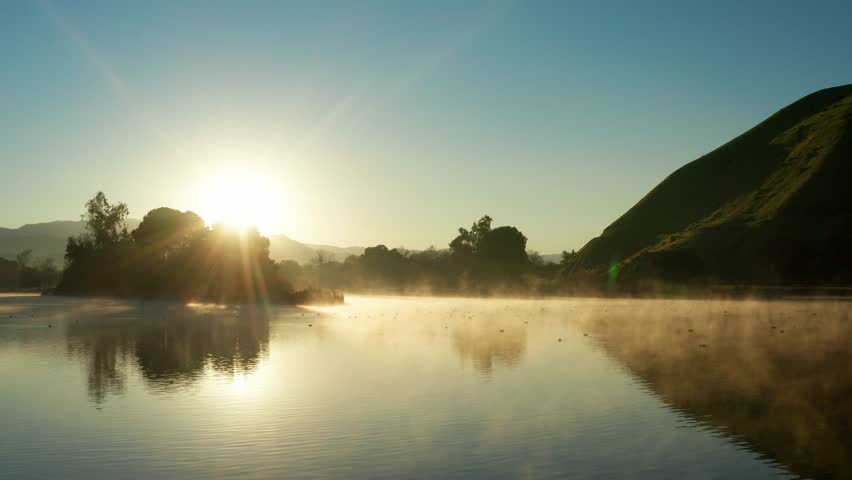 Fog drifting over shimmering Hart Park Lake in golden sunrise, spring morning