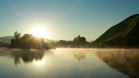 Fog drifting over shimmering Hart Park Lake in golden sunrise, spring morning
