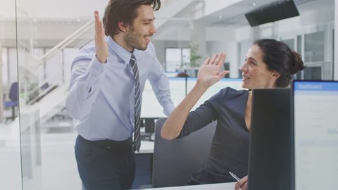 Two Professional Office Workers Work on Desktop Computer, Together Find Solution to a Problem and Cheerfully Celebrate Success by Doing High Five. Diverse Team of Beautiful People in Open Space Office