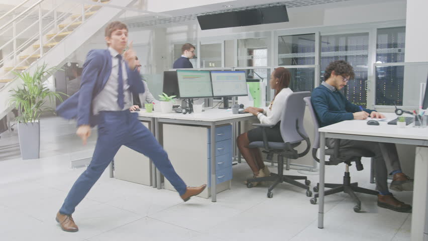 Young Fun Loving and Handsome Businessman Fooling Around, Dances Through the Open Space Office Hallway. Diverse and Motivated Business People Work on Desktop Computers Royalty-Free Stock Footage #1028088392