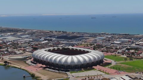 Port Elizabeth, South Africa - circa 2010s: Aerial hyperlapse, orbit around Nelson Mandela Bay Stadium on a sunny summer day. See harbour, industrial area, traffic come alive around the stadium.