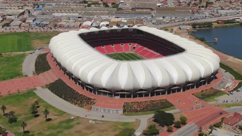 Port Elizabeth, South Africa - circa 2010s: Close up aerial orbit of Nelson Mandela Bay Stadium, looking through the roof, seeing goal posts on soccer field on a sunny summer day