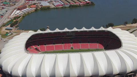 Port Elizabeth, South Africa - circa 2010s: Aerial view Nelson Mandela Bay Stadium, slow orbit, pull back into wide landscape shows stadium next to lake with city and Uitenhage mountains in background