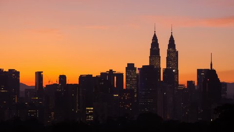 Time lapse: Silhouette of cityscape view during golden dawn overlooking the Kuala Lumpur city skyline from afar with yolk sun and lushes green in the foreground. Malaysia.