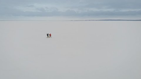 Aerial view of a two guys trekking in nature. Frozen river covered with thick layer of snow.