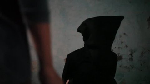 Dolly shot of a man wearing green colored t-shirt and moving towards the other man which is wearing black colored attire with a bag covering his face.