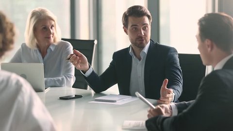 Businessman in suit talking to business people colleagues or partners sitting at conference table, male leader discussing work at team meeting or group negotiations having conversation with clients