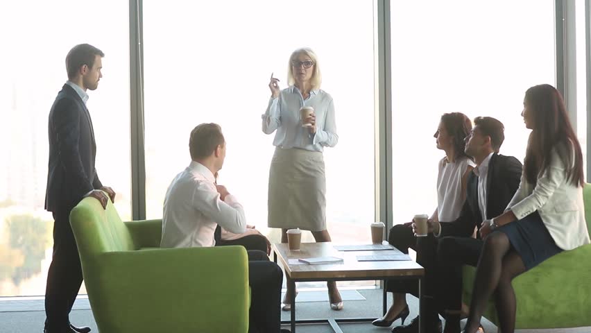 Friendly female mature old leader talking to diverse workers clients group at coffee break, business people team colleagues having fun conversation with middle aged boss discussing work in office Royalty-Free Stock Footage #1028099159