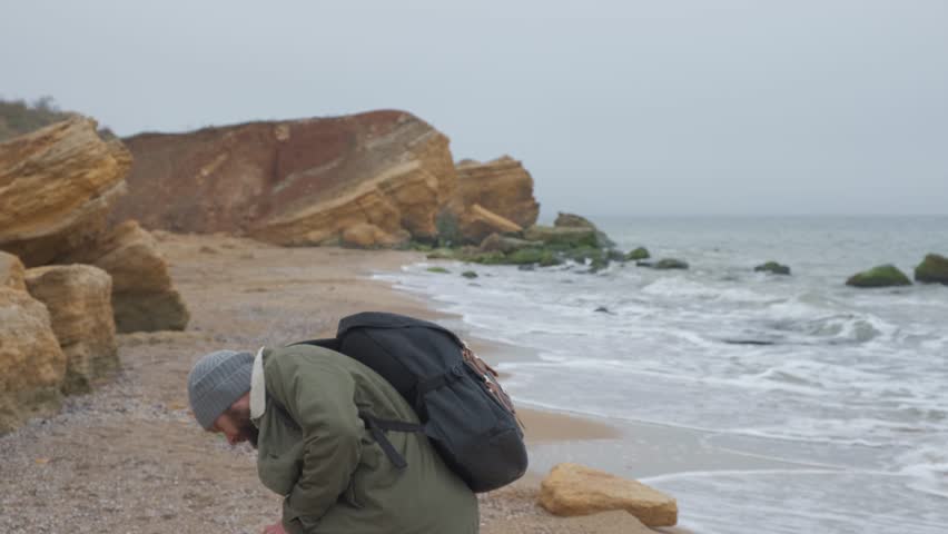 Young bearded man throws stones at the water in the evening.