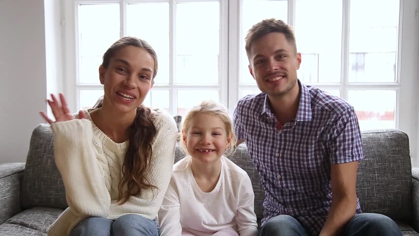 Happy family with little daughter sitting on couch at home waving hands look at camera talking at webcam say hello greeting friend or relatives, vloggers makes online video call recording vlog concept Royalty-Free Stock Footage #1028104286