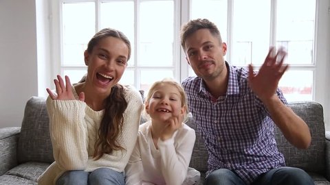 Happy family with little daughter sitting on couch at home waving hands look at camera talking at webcam say hello greeting friend or relatives, vloggers makes online video call recording vlog concept