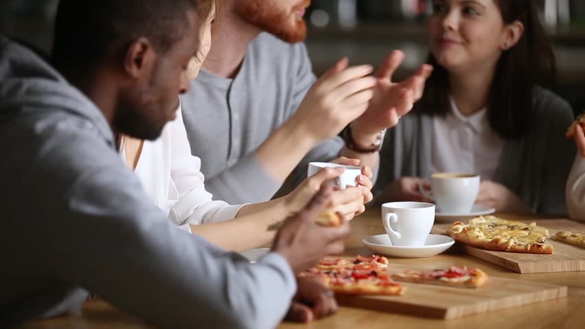 Millennial multinational friends students or colleagues gathered in cafe or pizzeria during lunch chatting enjoy conversation eating pizza drinking coffee or tea, group listens redhead guy share news Royalty-Free Stock Footage #1028104298