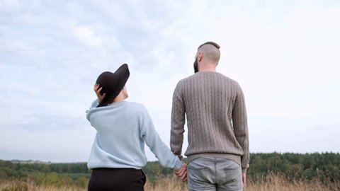 Young beautiful couple in sweaters and hats against the background of nature, fields with green grass and forest. Short hair and dyed hair. Love and hugs.