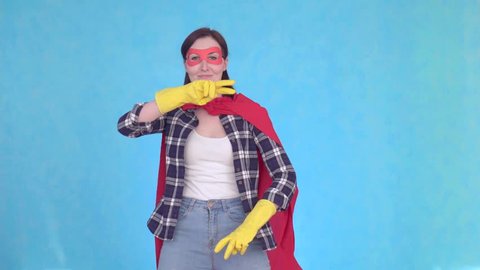 Young superhero woman housewife dancing on blue background