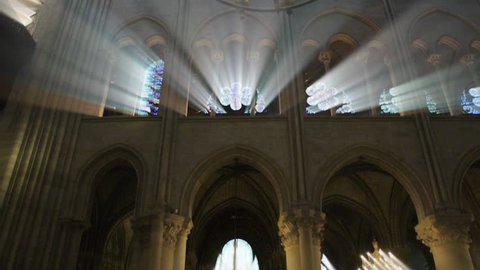 Paris, France - Circa 2017: Majestic holly light beams through windows columns and stained glass windows with rooftop and magnificent chandelier of Notre-Dame de Paris cathedral with visitors tourists