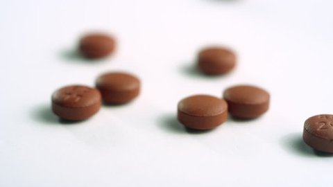 Close-up of scattered brown ibuprofen pills, spinning right out of focus on a white surface