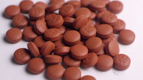 Close-up of a pile of brown ibuprofen pills, spinning right on a white surface