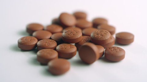 Close-up of a pile of brown ibuprofen pills, spinning left on a white surface