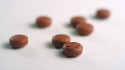 Close-up of scattered brown ibuprofen pills, spinning left out of focus on a white surface