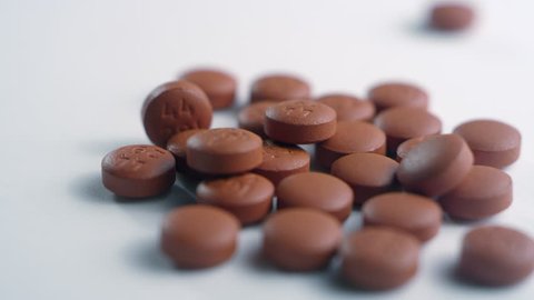 Close-up of a pile of brown ibuprofen pills, spinning left on a white surface