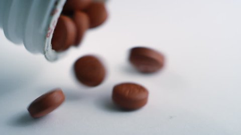 Close-up of brown ibuprofen pills getting poured out of a pill bottle on a white surface