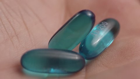 Macro close-up of a pile of blue ibuprofen liquid gel pills dropping into a human hand