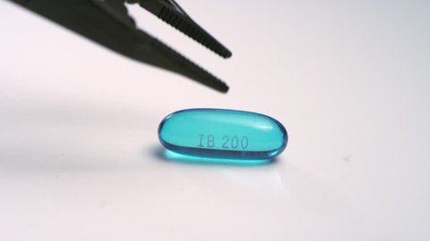 Close-up of a single blue ibuprofen liquid gel pill getting picked up by a tool on a white surface