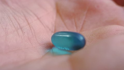 Macro close-up of a single blue ibuprofen liquid gel pill dropping into a human hand