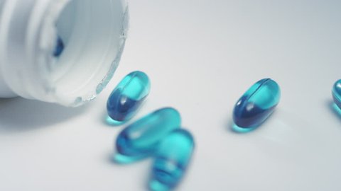 Close-up pan right on a pill bottle of blue ibuprofen liquid gel pills scattered on a white surface