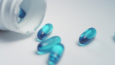 Close-up pan around a pill bottle of blue ibuprofen liquid gel pills scattered on a white surface