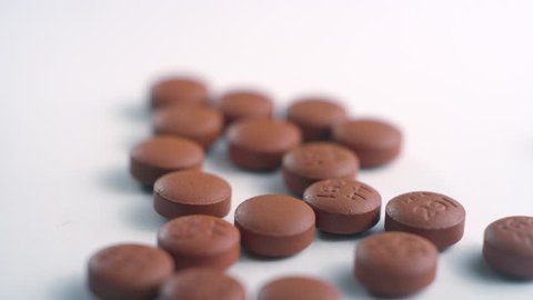 Close-up of brown ibuprofen pills getting poured out of a pill bottle and scattering on a white surface