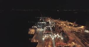 4K aerial video with high angle view of a maritime container port with big cranes and trucks unloading containers from cargo ship at night in Oslo, Norway.