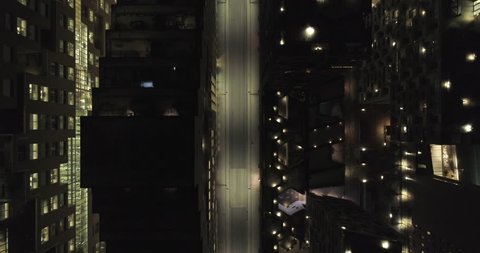 4K aerial video with downward motion and a birds eye view of the dark rooftops of financial- and apartment buildings and an illuminated empty street at night in downtown Oslo, Norway.
