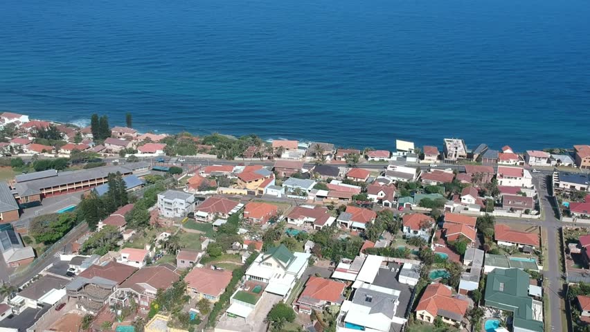 Ascending aerial view of a residential area on a hillside near the coast. Beautiful azure sea and bright sky on the horizon. Scenic beauty of Durban, South Africa.