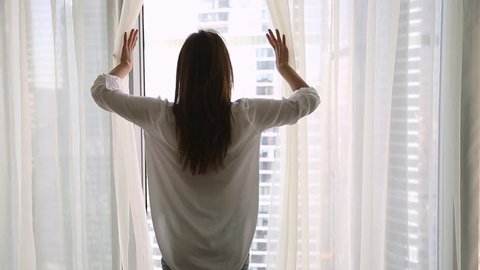 Woman in white shirt and jeans opens curtains in the morning big city modern skyscrapers view through panoramic window, traveller woke up in luxury hotel room, wellbeing welfare, start the day concept