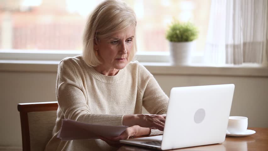 Elderly stressed woman sitting at table in kitchen at home holds domestic bills use laptop makes online payments feels concerned forgot to pay or debt formed, check finances financial problems concept Royalty-Free Stock Footage #1028137070
