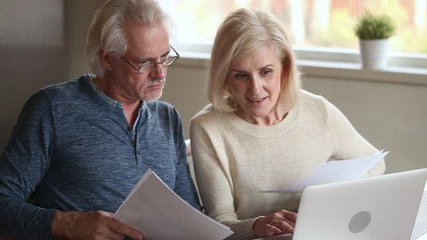 Elderly couple holds bills makes online payment use pc, check bank account balance feels satisfied, wife explains help to husband do transaction, easy secure money remittance modern tech usage concept