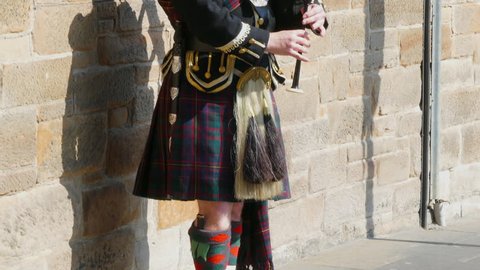 EDINBURGH, SCOTLAND, APRIL 19TH 2019: Scottish piper playing bagpipes solo on an unusually warm and sunny Easter day. Pan shot down the traditional outfit of kilt and sporran to foot tapping in boots.