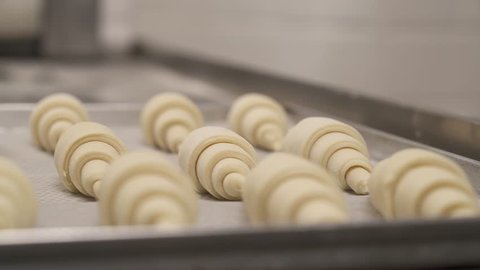 Left to right close-up shot of laminated dough rolled into croissants in the foreground. Pastry chef rolls viennoiserie dough to make a croissant. Professional food making concept