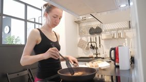 Young woman standing by the stove in the kitchen and preparing breakfast for the family, lifestyle video. Everyday family life.